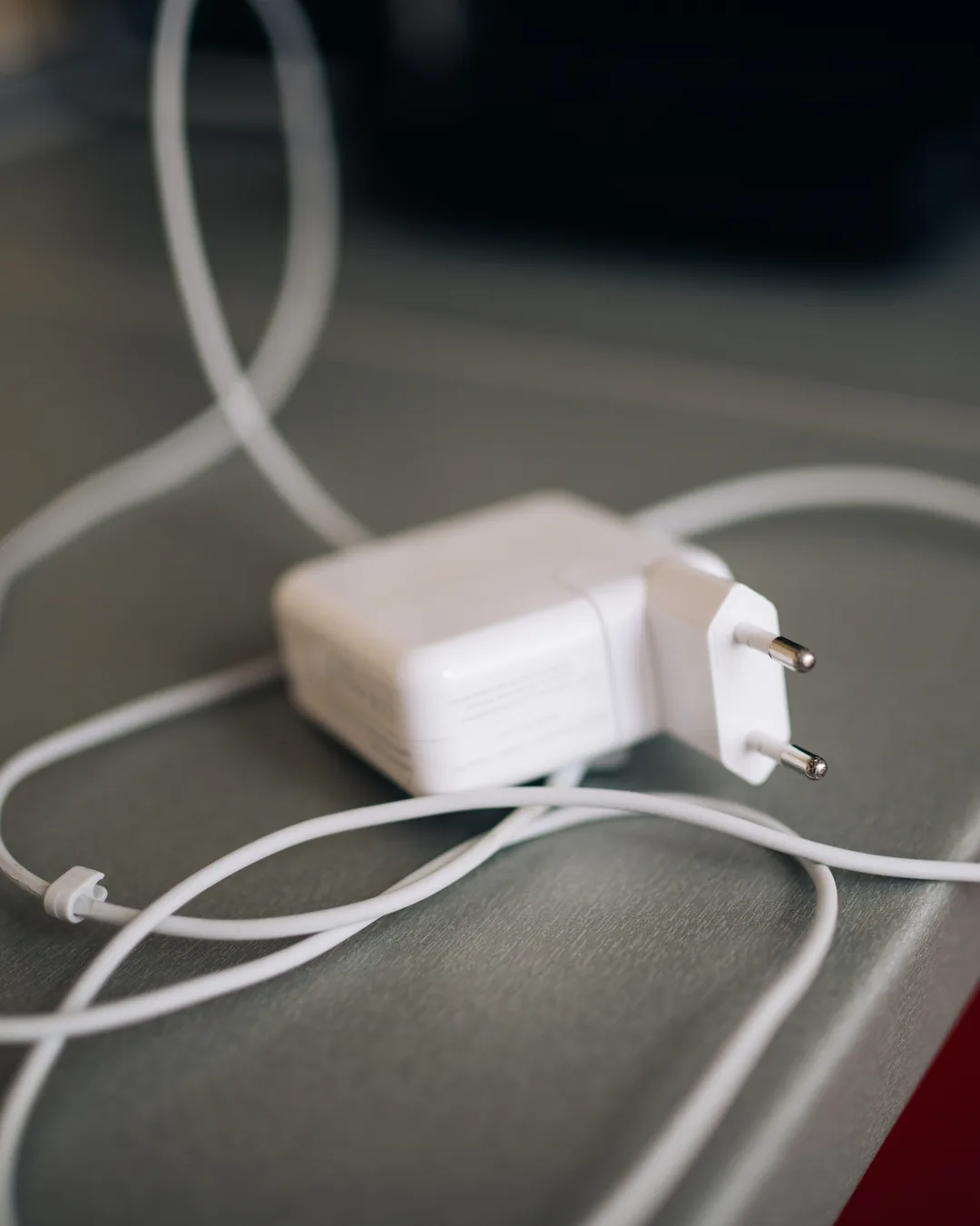 Cargador de pared blanco con enchufe europeo y cable enrollado sobre una mesa gris, con luz de día