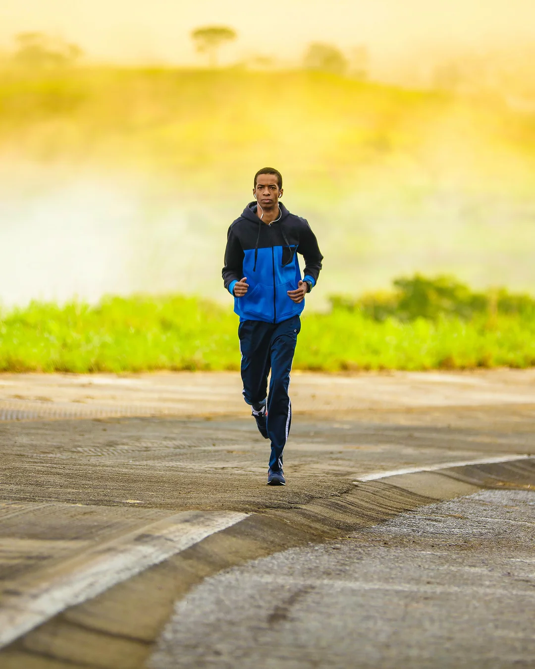 Hombre con chándal azul corriendo por el arcén de una carretera