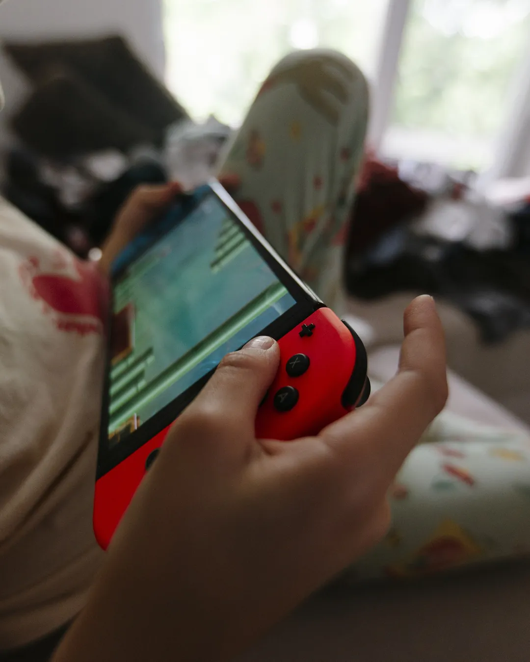 Niño sentado en un sofá con una consola portátil de mandos rojo y azul en las manos, de espaldas y con la pantalla encendida