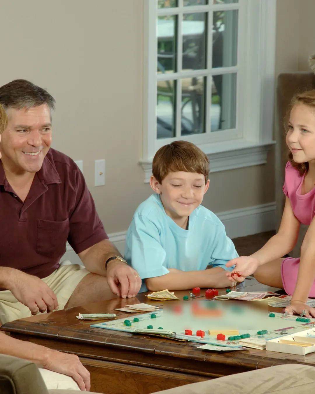 Padre, hija e hijo sentados alrededor de una mesa baja del salón, jugando a un juego de tablero y sonriendo