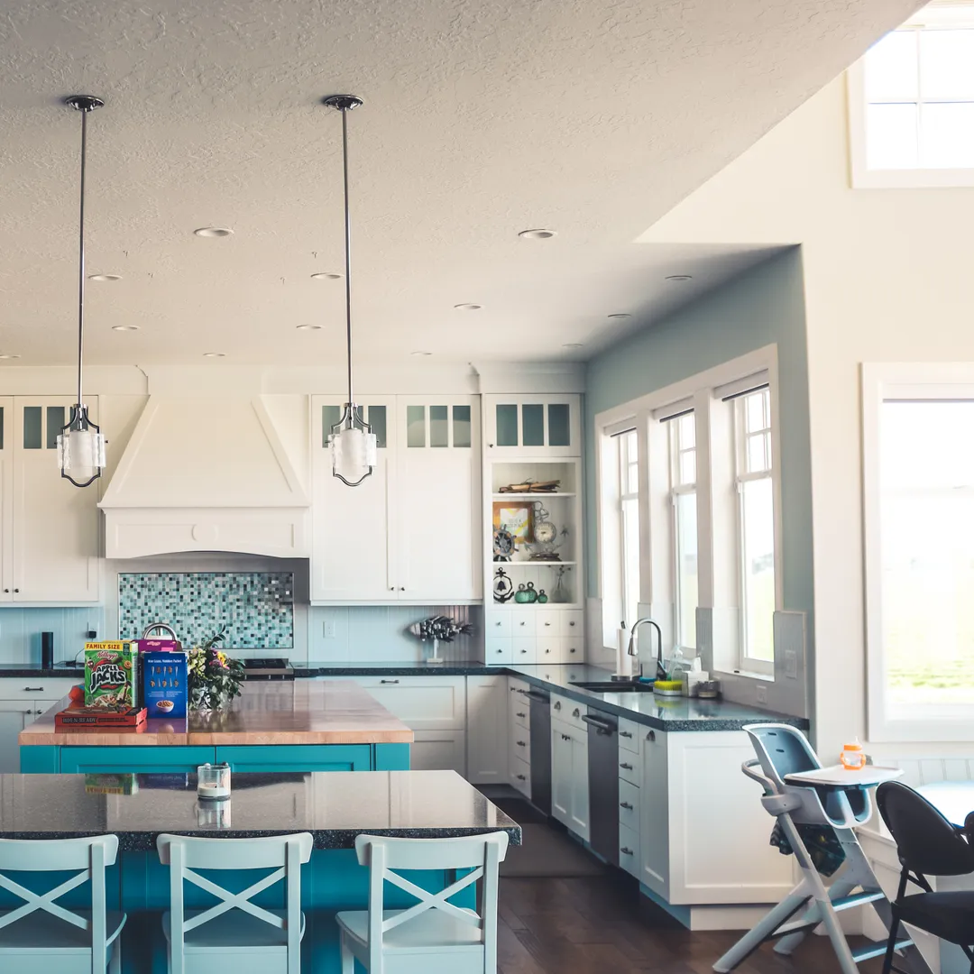 Cocina luminosa en blanco y azul con isla, taburetes y lámparas colgantes