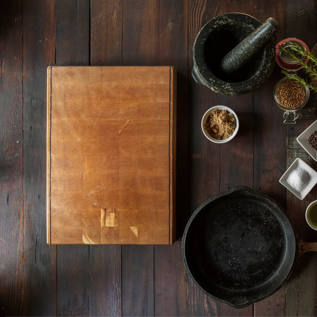 Tabla de cortar, sartén de hierro, mortero y especias sobre una mesa de madera oscura
