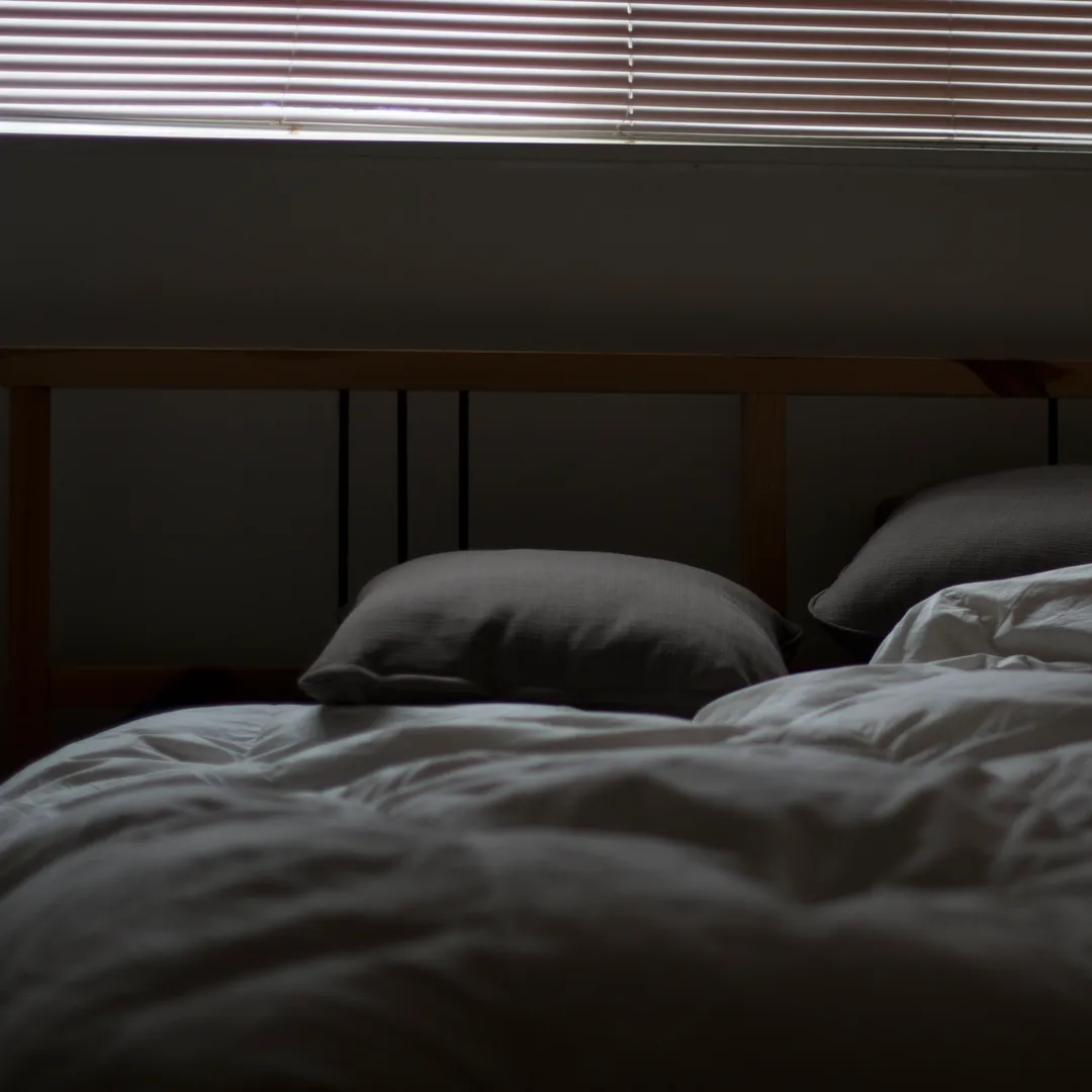 Cama deshecha con sábanas y almohadas oscuras y persianas cerradas