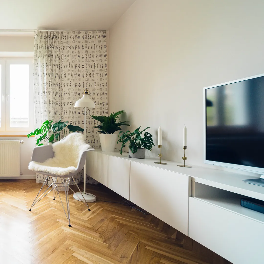 Salón blanco con suelo de madera, plantas, un sillón y un mueble bajo