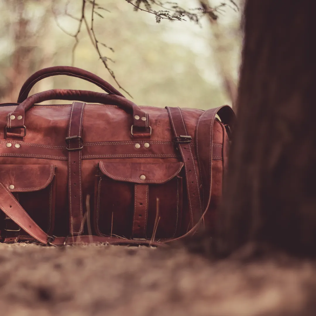 Bolsa de viaje de cuero marrón sobre el suelo de un bosque