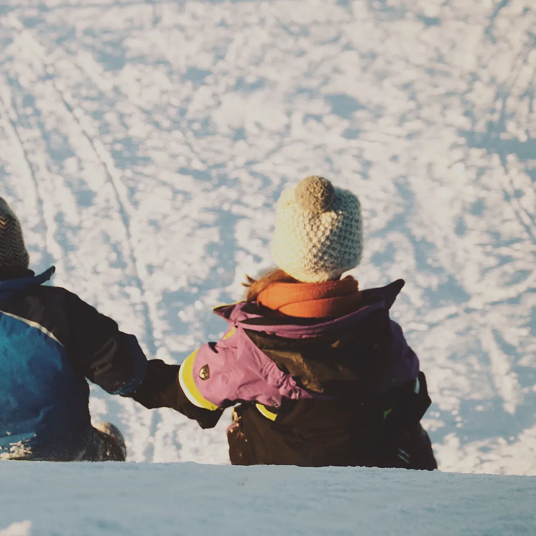 Dos niños con ropa de abrigo y gorros de lana sentados en la nieve