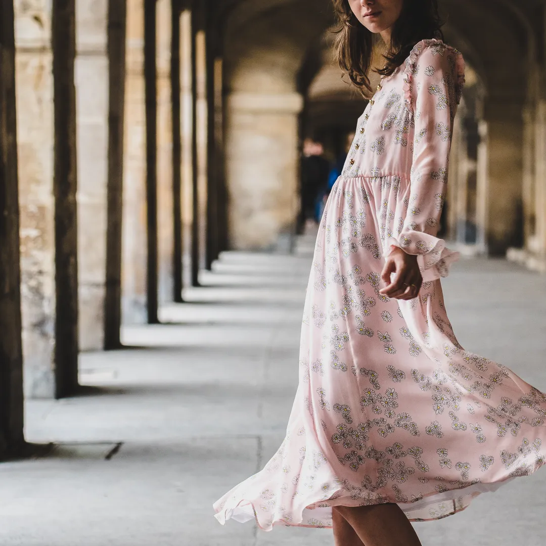 Mujer con vestido largo de flores caminando bajo unos soportales