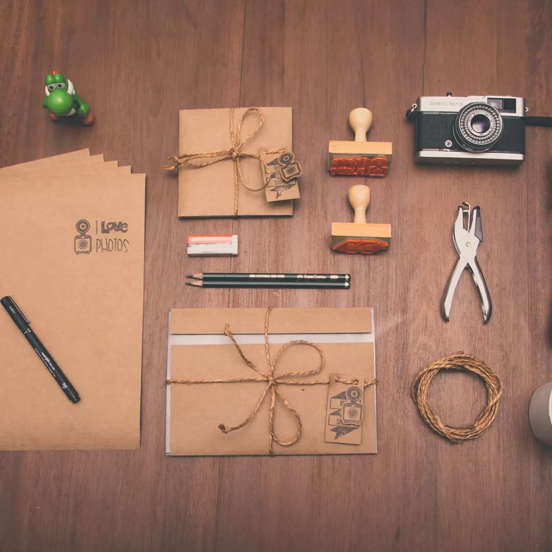 Material de papelería ordenado sobre una mesa de madera: sobres, sellos, tijeras y cordel