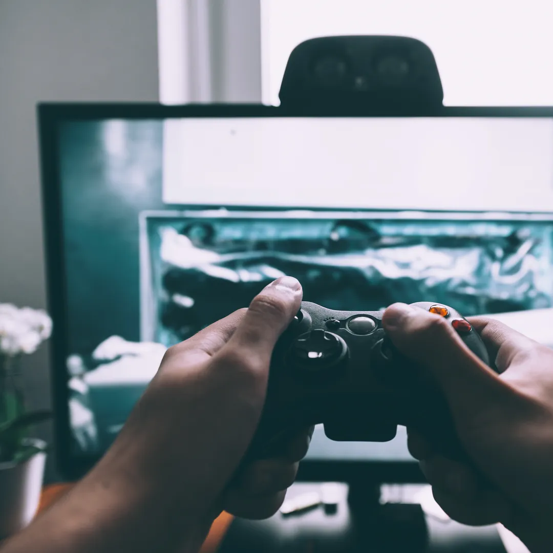 Manos sujetando un mando de videoconsola delante de una pantalla