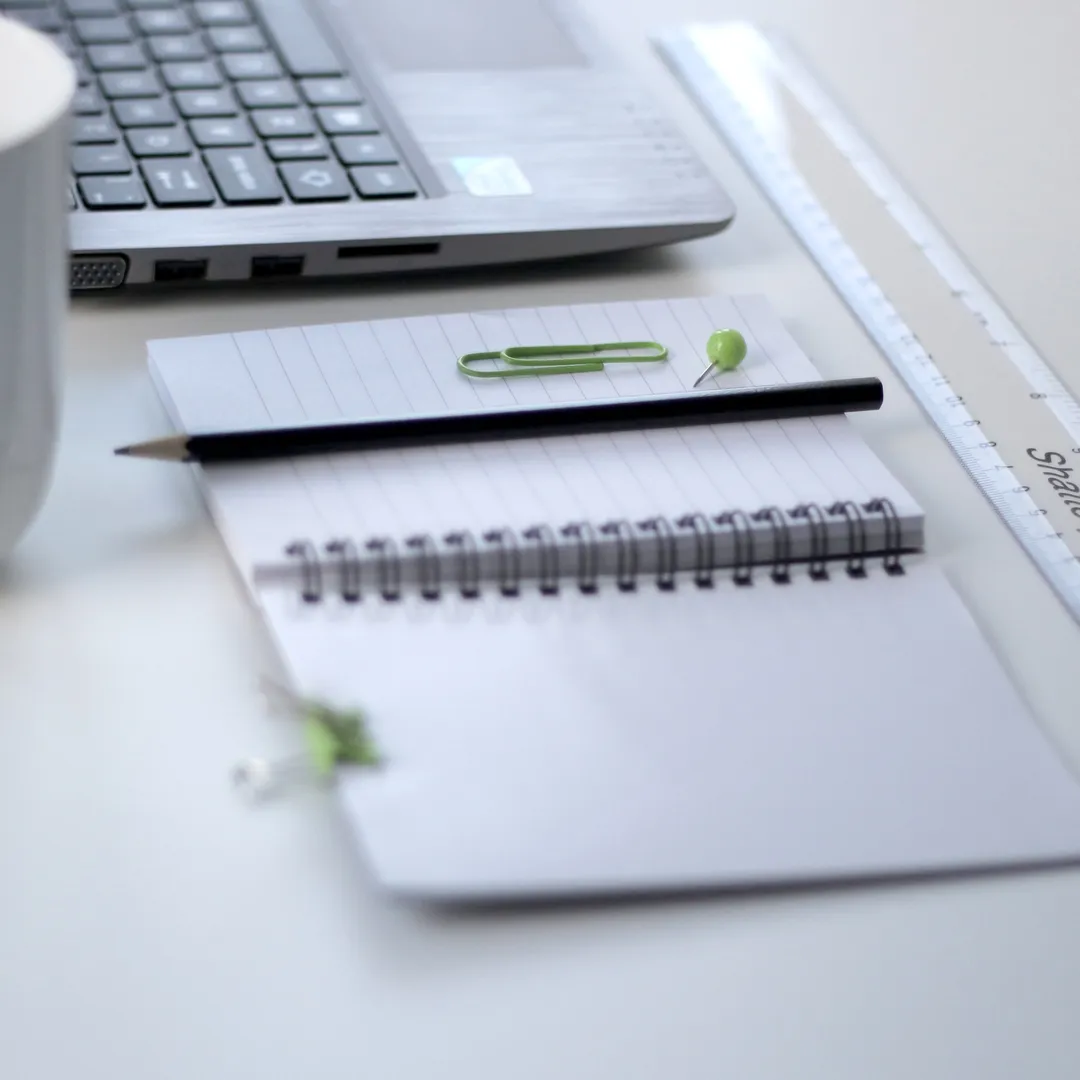 Portátil, cuaderno de espiral y bolígrafo sobre una mesa blanca