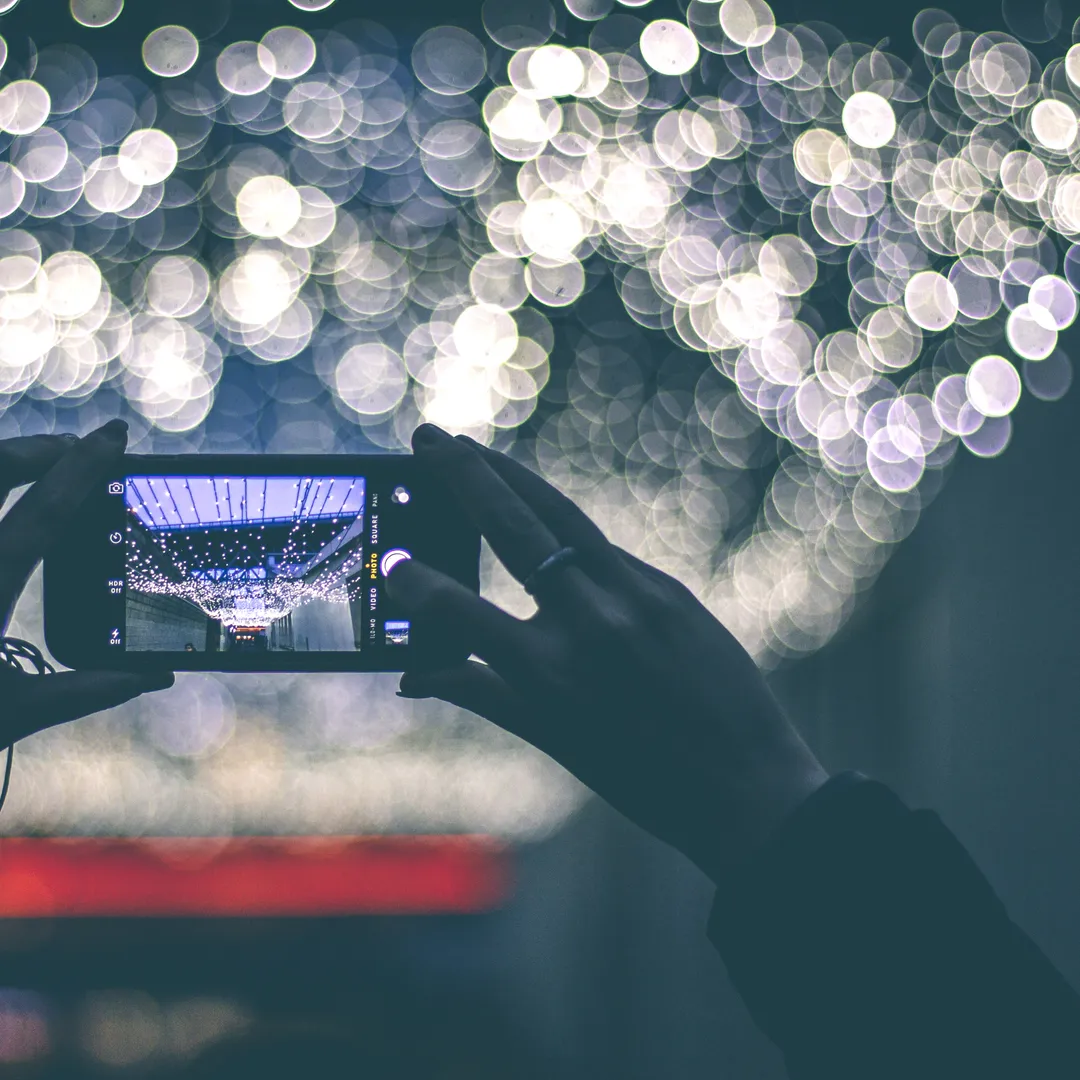 Manos sujetando un móvil que fotografía luces desenfocadas