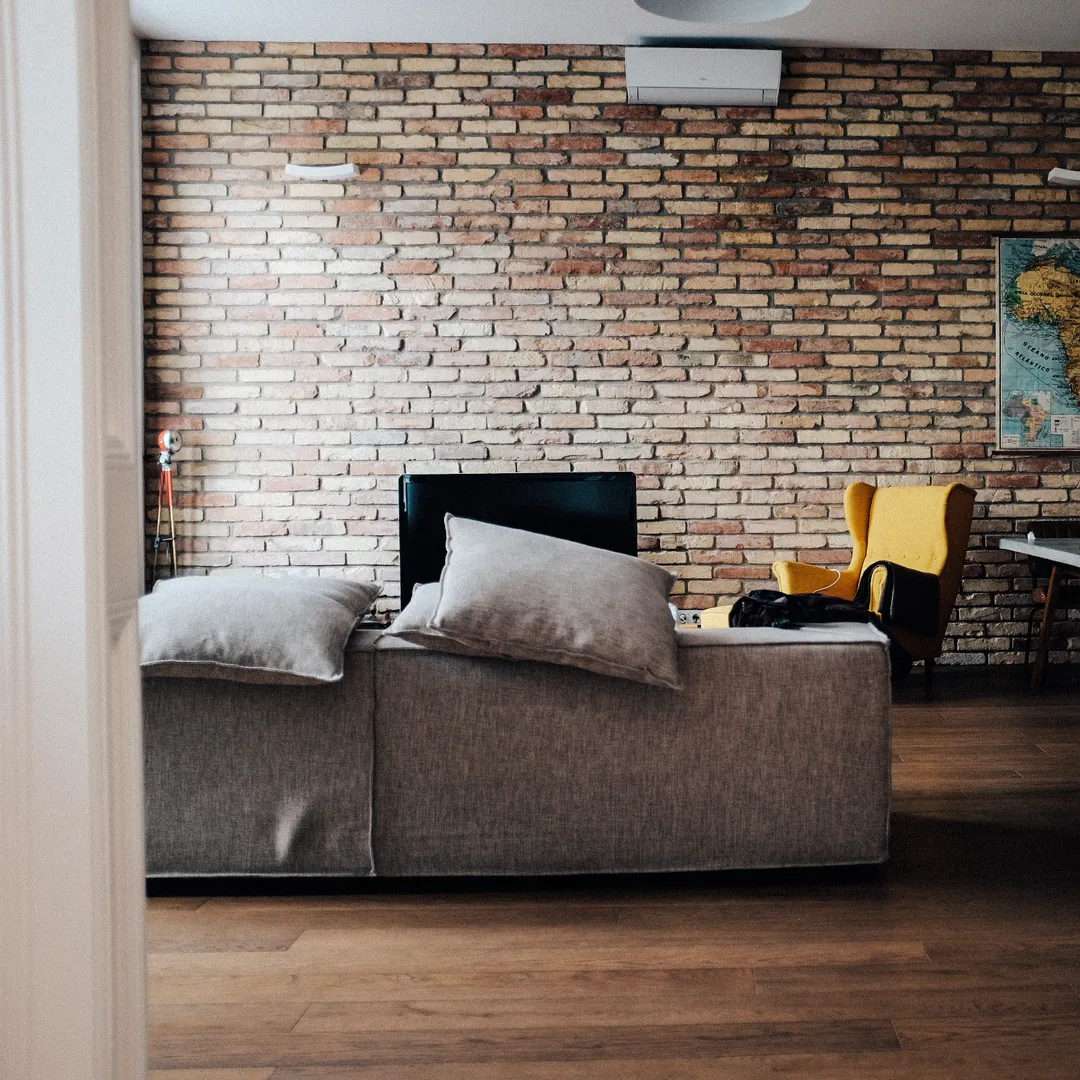 Salón con pared de ladrillo, sofá gris y un televisor