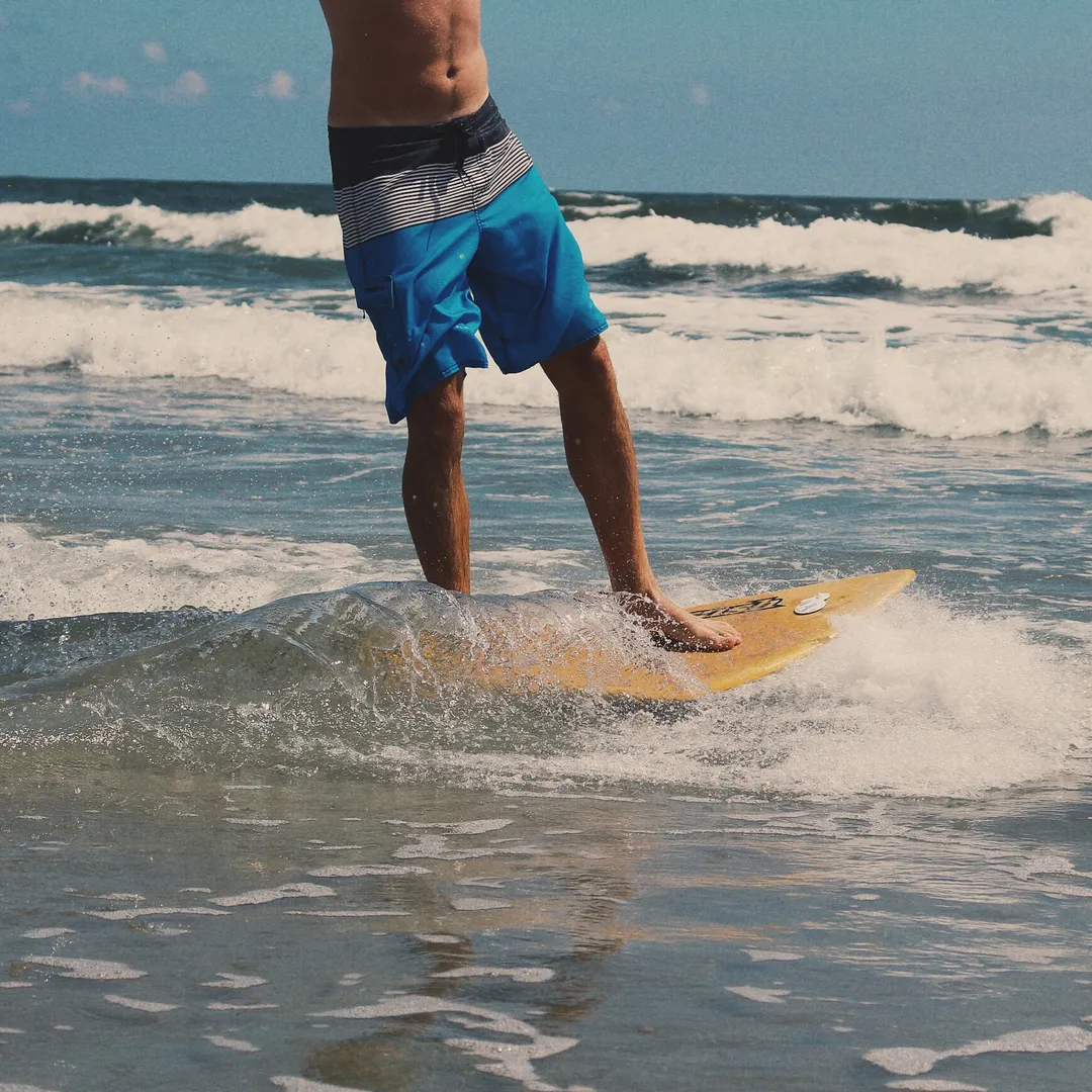 Piernas de un surfista con bañador azul entre las olas