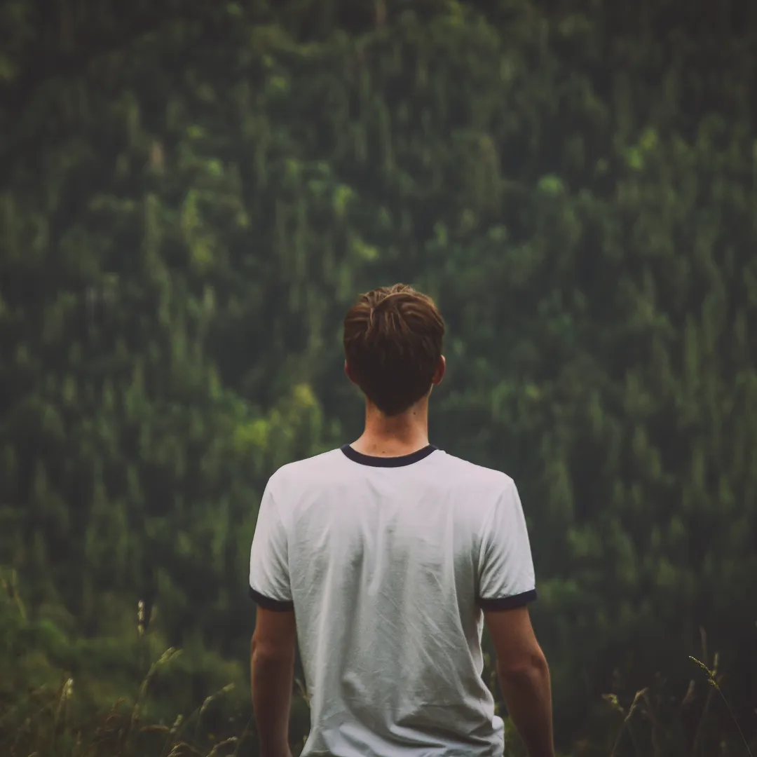 Hombre de espaldas con camiseta blanca frente a un bosque