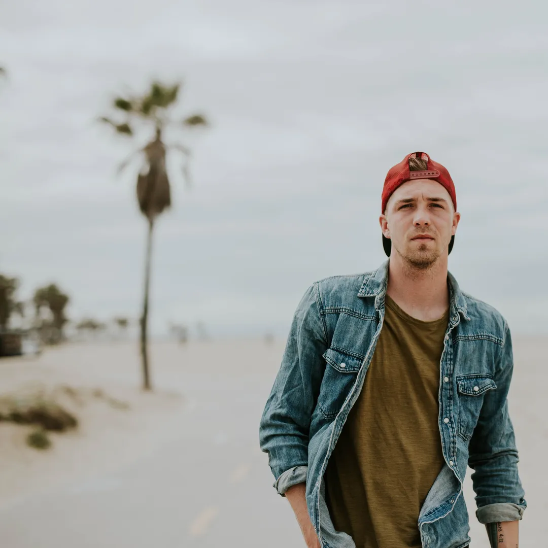 Hombre con chaqueta vaquera y gorra en una playa