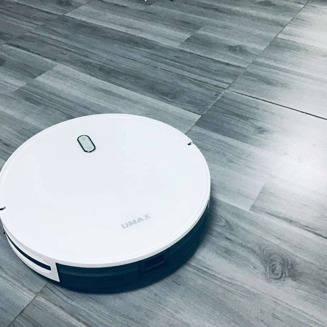 Robot aspirador blanco sobre un suelo de tarima gris