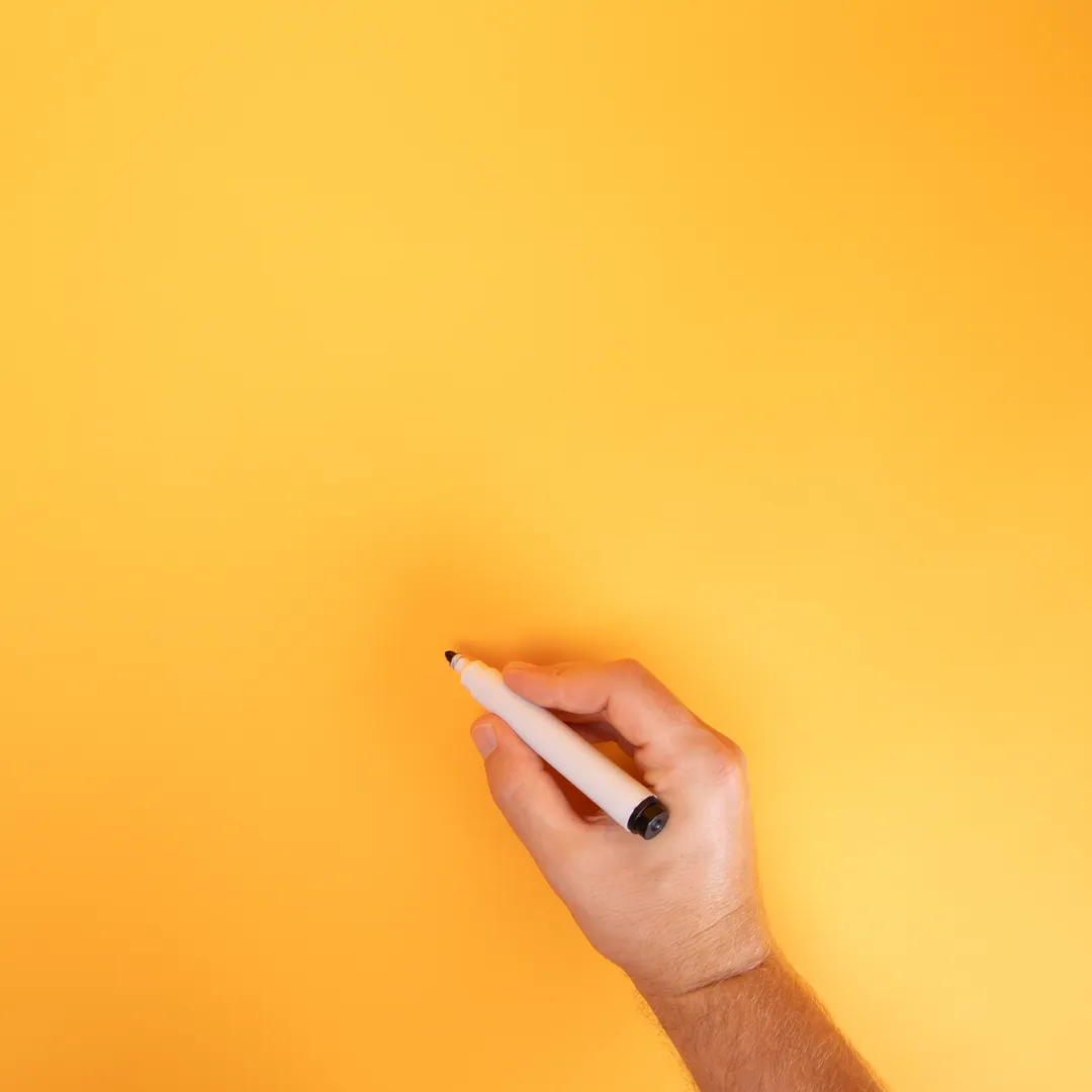 Mano escribiendo con un rotulador negro sobre fondo naranja