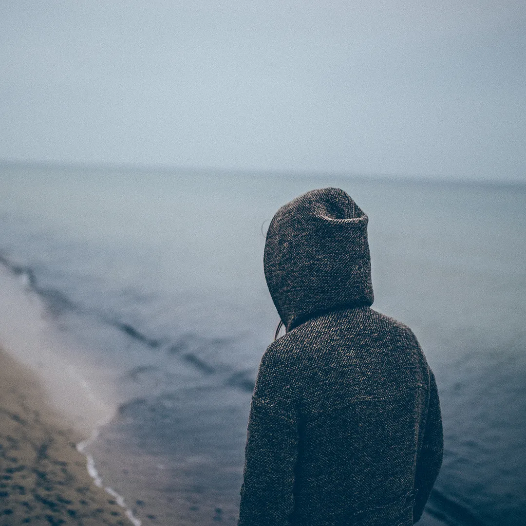 Persona de espaldas con sudadera con capucha mirando el mar